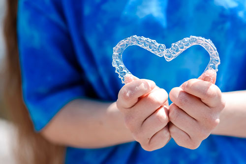 Woman holding clear aligners, forming a heart shape